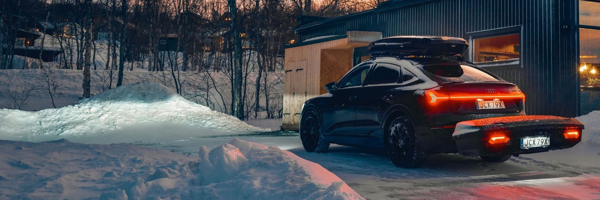 配備 Thule 車頂箱和 Thule Arcos XL 的汽車，停在白雪皚皚的冬季景觀中。