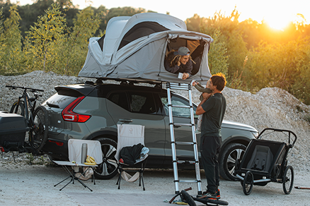 Tenda soft-shell in campeggio. Una donna in una tenda sul tetto e un uomo che porta in braccio un bambino