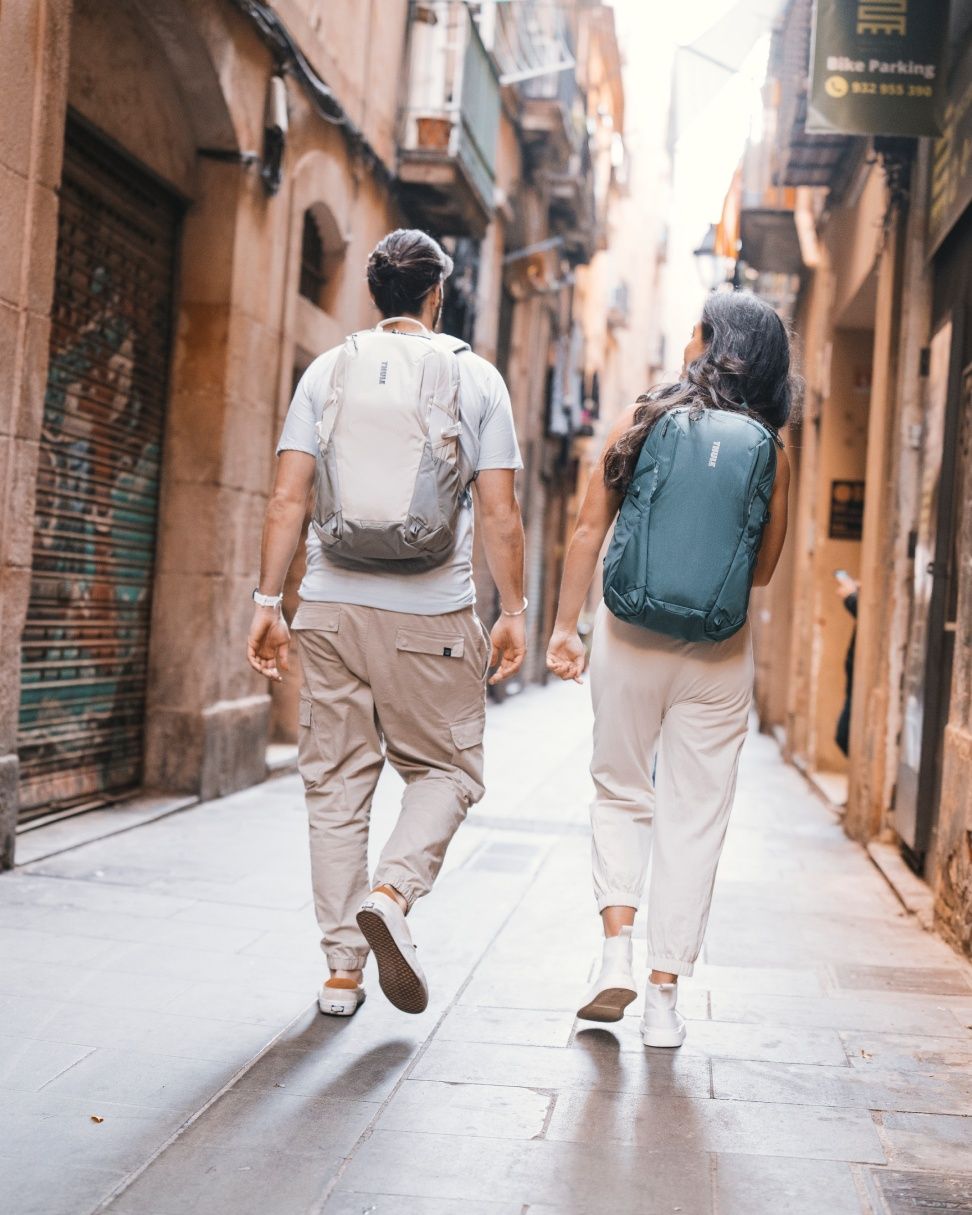 Two people walk down a narrow alleyway in the city carrying Thule Enroute backpacks. 