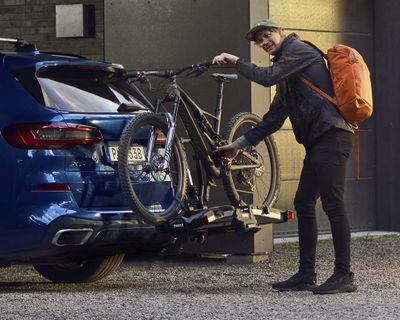 A man with an orange backpack unloads his bike from a hitch bike rack.