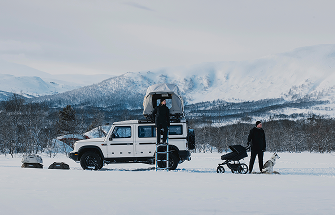 Een auto geparkeerd in een winterlandschap, geladen met een tent op Thule-dak