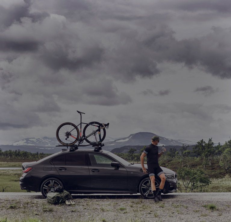 On a mountain road two cyclists unload their bikes from a Thule roof bike rack.