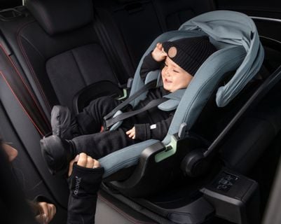 A baby sitting in a Thule car seat smiles while a woman interacts with it.