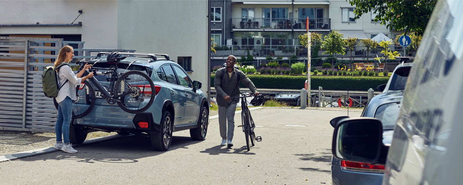A woman unloads her bike from a Thule car mount for bike while a man with a bike walks towards her.
