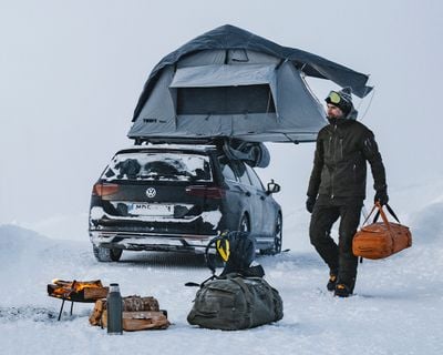 Una persona cammina davanti a un'auto parcheggiata nella neve con una tenda da tetto.