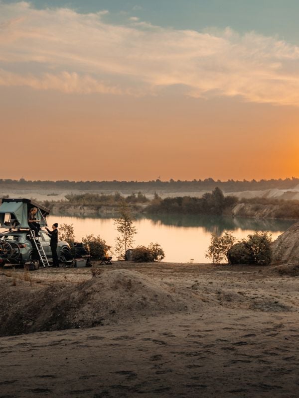Een man en een vrouw maken een tent en een campingplaats op het dak van een auto klaar voor de nacht.