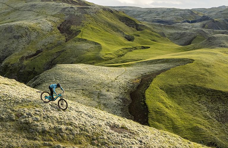 A woman rides a her bike through the rugged Icelandic countryside with a Thule Vital hydration pack.