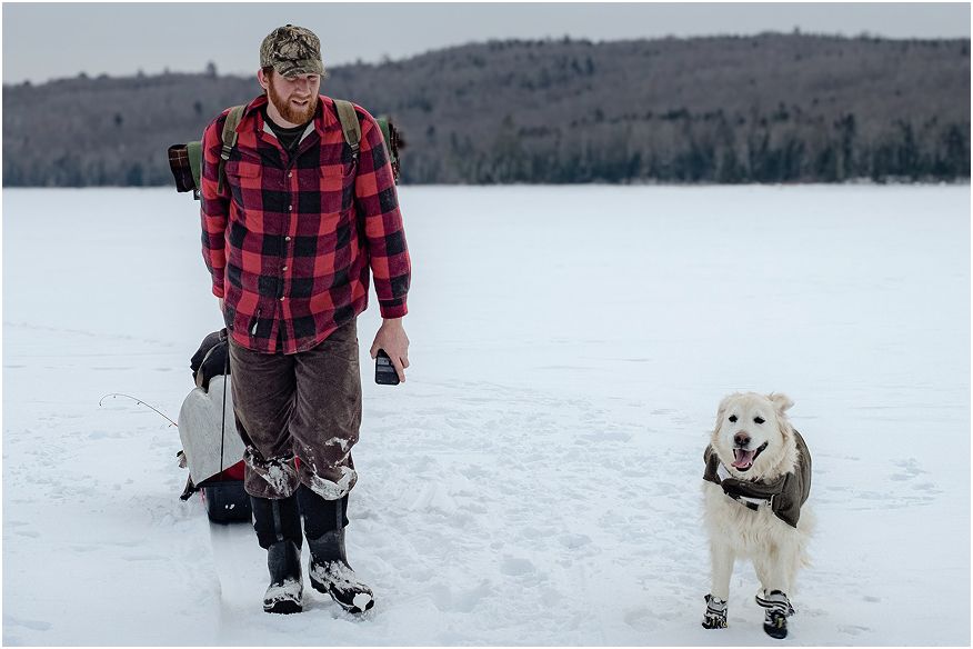 Dan Caridi pulling a gear sled across a frozen lake with his dog on a winter fishing trip.