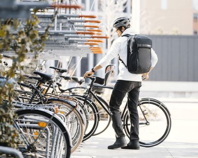 Thuleの通勤用バックパックを背負い、バイクラックに自転車を積み込む男性。