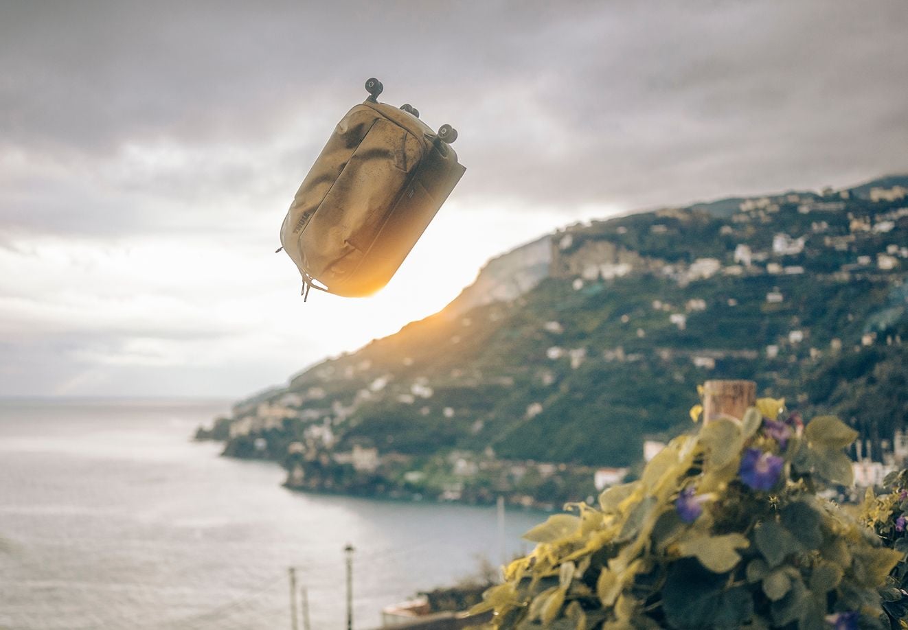 En Thule Aion-sekk ser ut som om den svever i luften mot et fantastisk kystlandskap ved solnedgang.