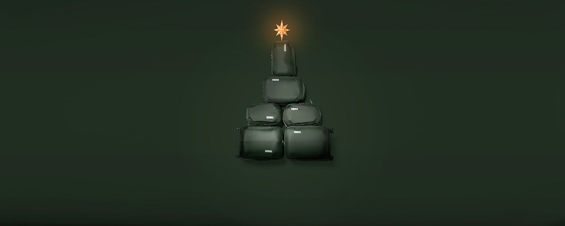 Fire grønne Thule Chasm rejsetasker er stablet i højden med en stjerne på toppen som et juletræ.