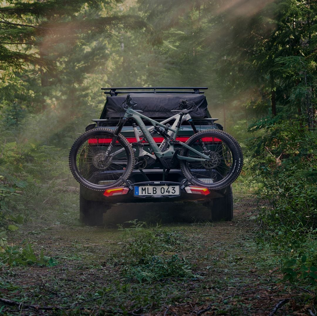 Thule Epos Fahrradträger, montiert auf einem Auto mit zwei Mountainbikes in einer Waldumgebung.