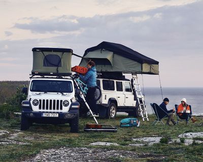 Two vehicles are parked near a cliff with soft and hard-shell roof top tents.