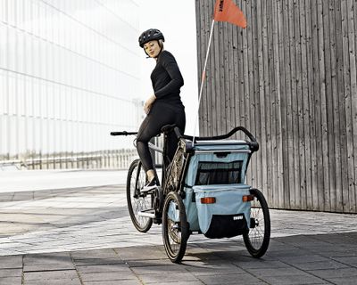 Een vrouw fietst door de stad met een kinderfietstrailer.
