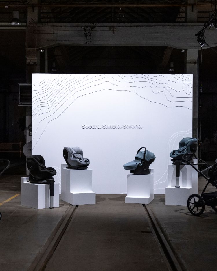 A big white screen with the words “Secure. Simple. Serene.” written on it. In front of it are four white columns with Thule Alfi car seat base, Thule Maple infant car seat, Thule Elm toddler car seat and a stroller.