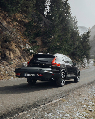 Um SUV preto com uma caixa de carga traseira Thule Arcos na traseira segue por uma estrada. 