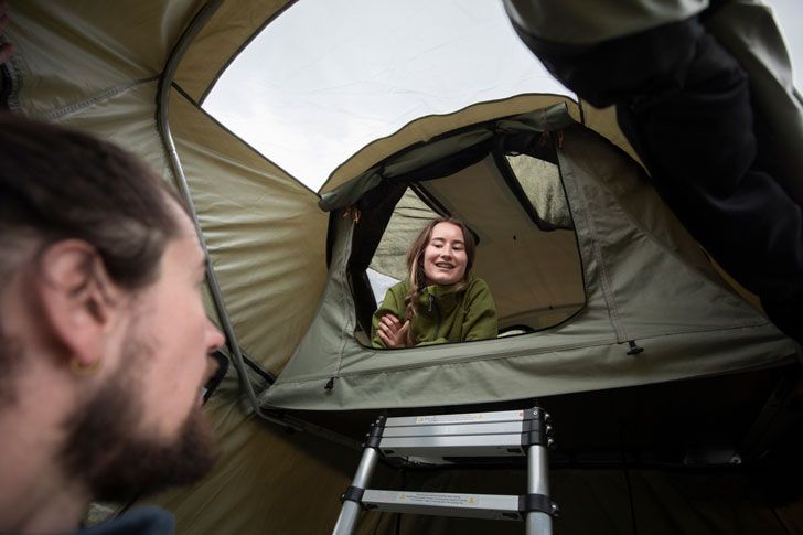 A man looks up at a woman sitting inside a Thule roof top tent.