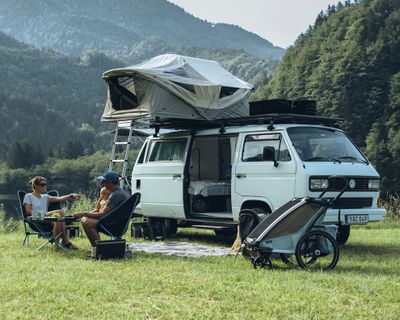 A van is parked in nature with a soft-shell roof top tent.