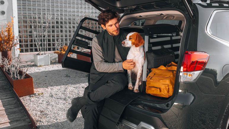 En mand sidder i bagagerummet på sin bil med sin hund.