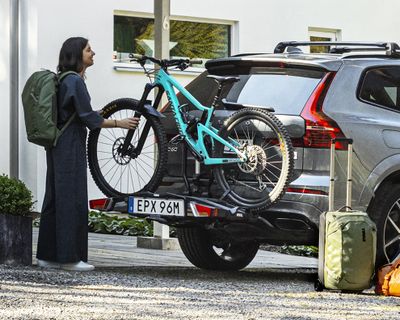 A woman with a green backpack unloads her bike from a towbar bike rack.