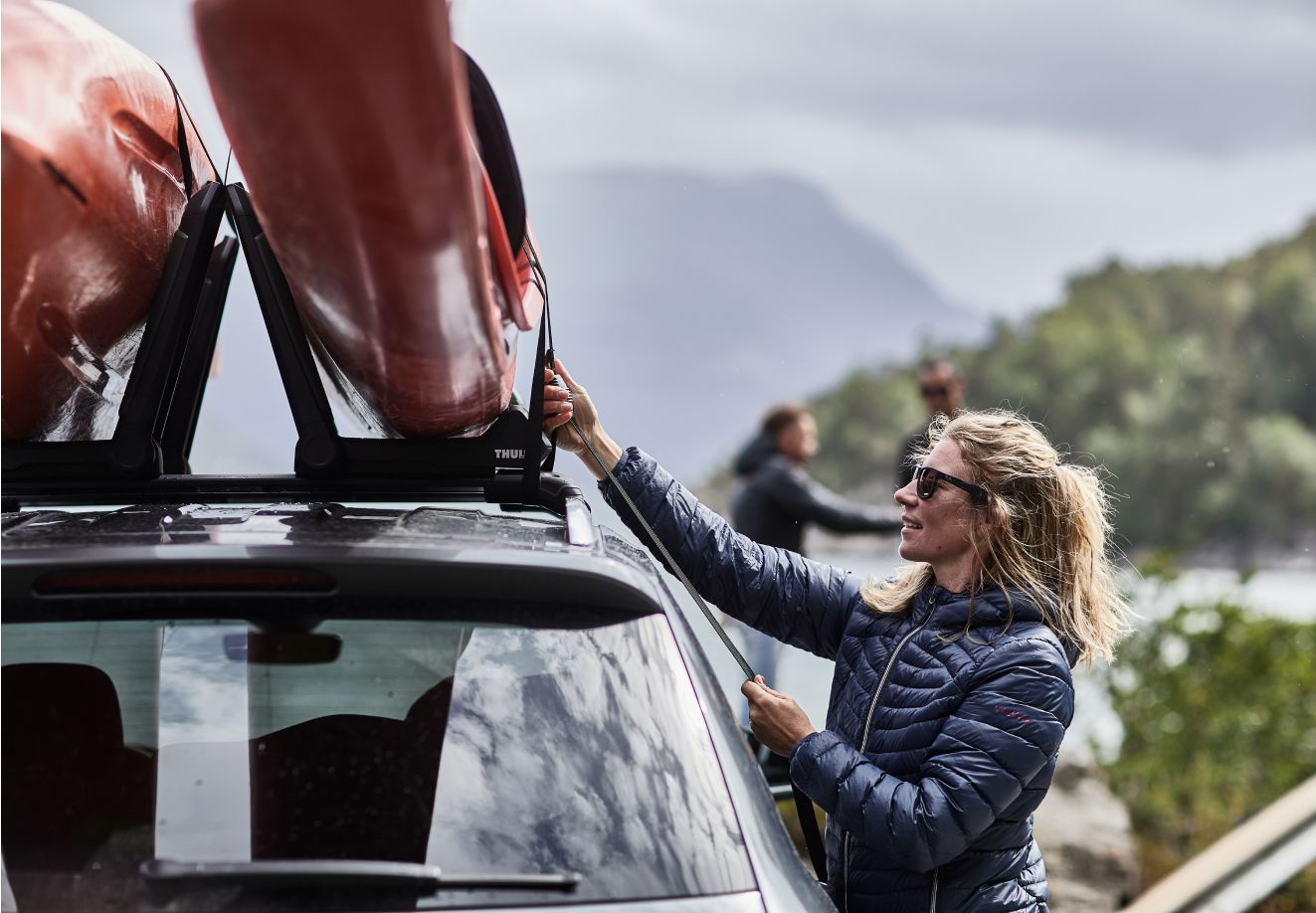 Uma pessoa fixa caiaques em um rack para caiaques Thule em cima de um carro.