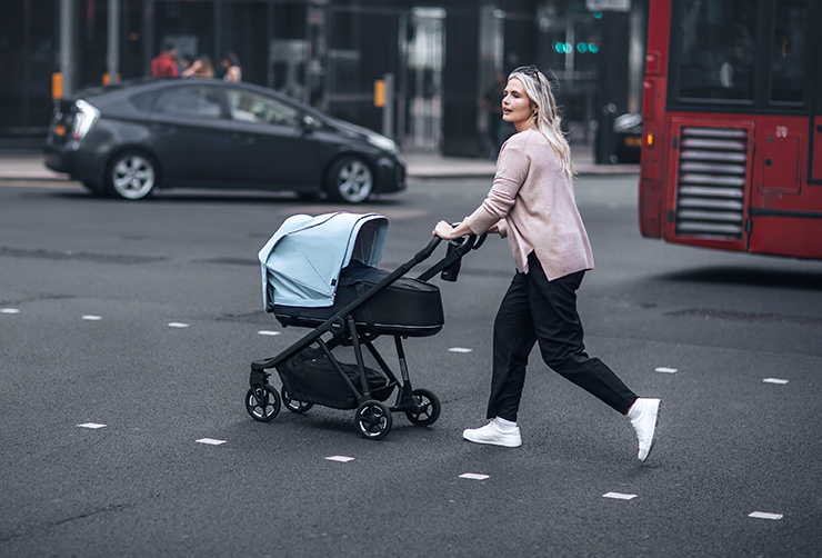 A parent walks across a crowded street with their toddler in a Thule Shine Air Purifier Canopy.