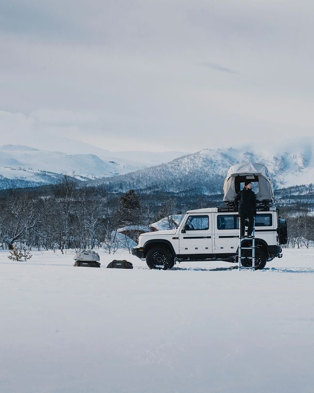 Un coche aparcado en un paisaje invernal, cargado con una tienda de techo Thule
