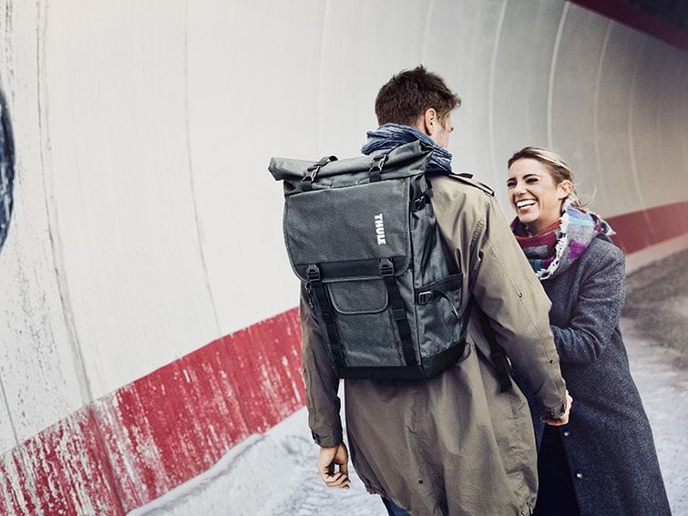 Standing in a tunnel, a woman laughs facing a man who is carrying one of Thule camera backpacks.