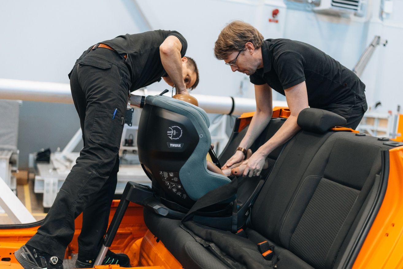 Due uomini posizionano un manichino bambino in un seggiolino da auto durante un test di sicurezza.