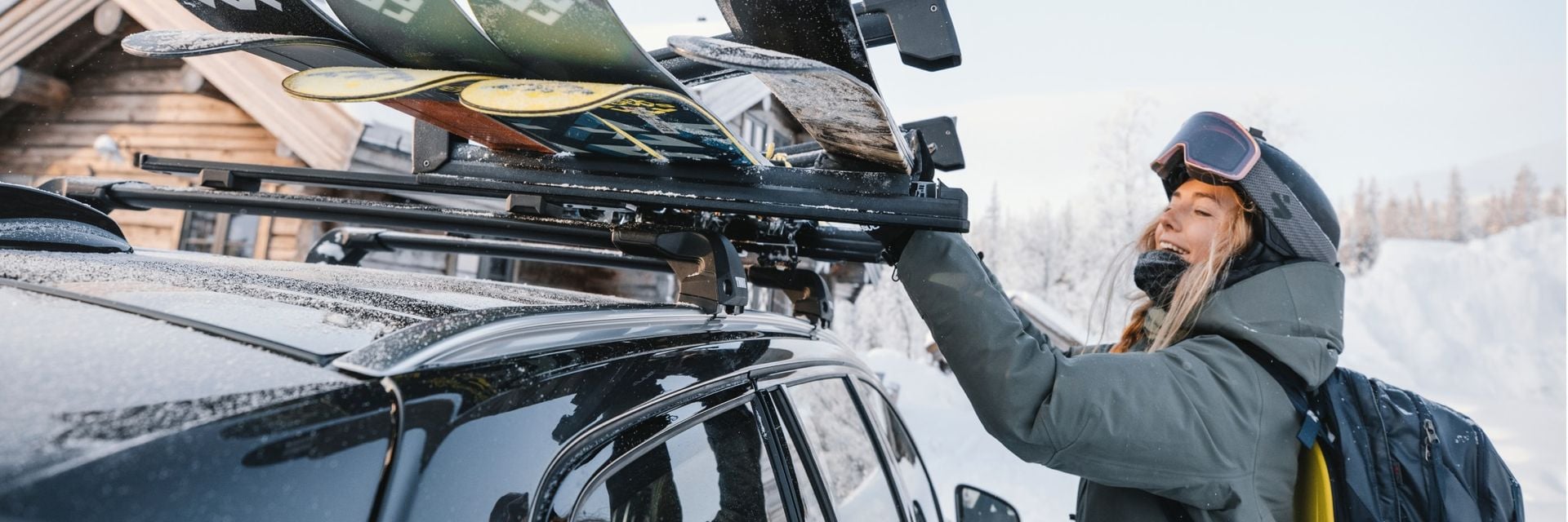 A woman removes skis from a Thule ski rack mounted to the roof of a car in the snow. 