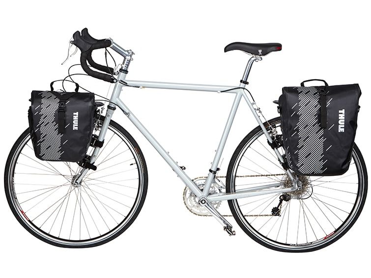 A blue city bike with black bike bags and a white background.