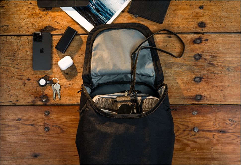 A Thule Subterra backpack is on a wooden table with items placed inside and around the bag.
