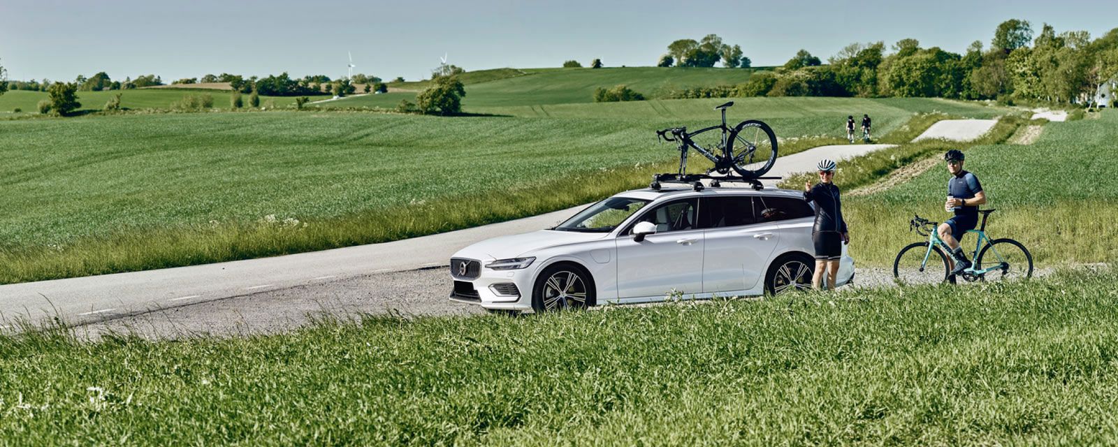 Two cyclists in a field prepare for a bike trip with their bikes loaded on a Thule roof bike rack.