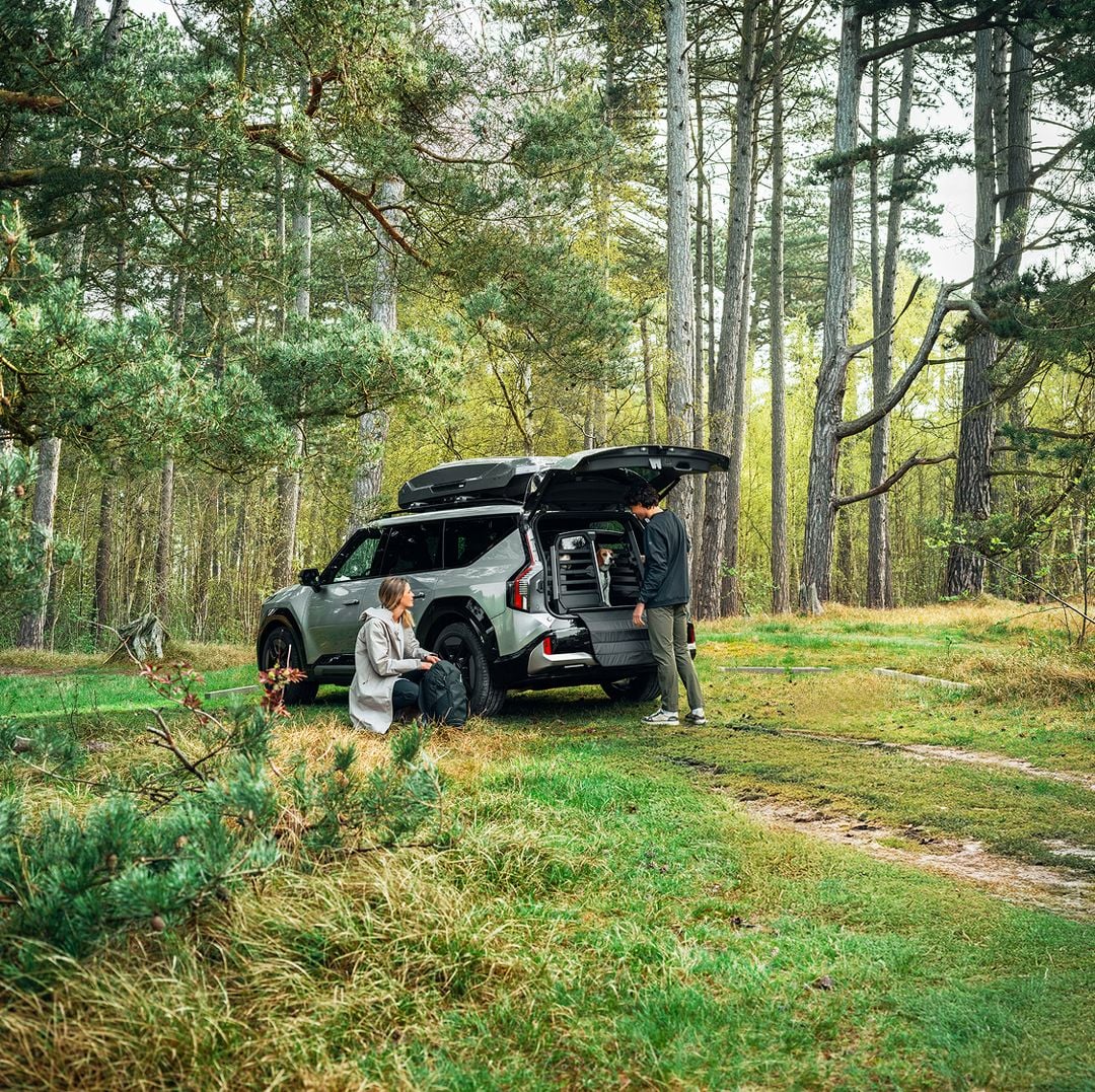 Duas pessoas descarregando equipamentos de um SUV com uma caixa de carga no teto em uma floresta.