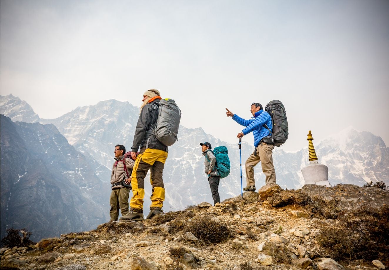 Vier mensen met een grote rugzak staan op een bergwand en een van hen wijst naar iets.