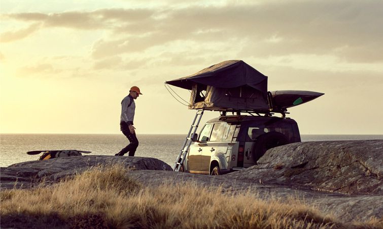 A man walks on the beach beside a car with a kayak and a Thule Tepui Foothill roof top tent.