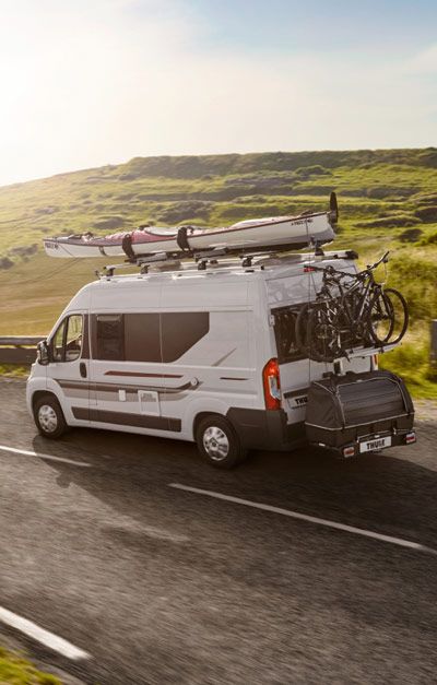 A van with a Thule van bike rack attached behind rides down a street towards the sea.