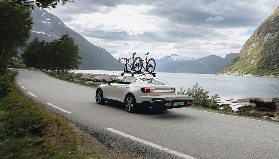 A car fitted with a rear-mounted cargo carrier driving with two bicycles mounted on the roof.