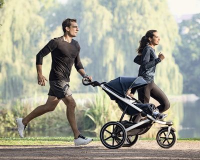 A couple run through a park with their Thule jogging strollers.