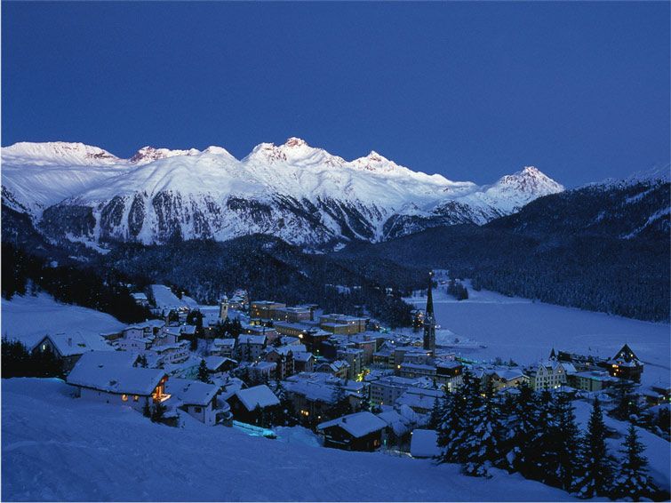 The ski village of St Moritz at the bottom of snow covered peaks at dusk.