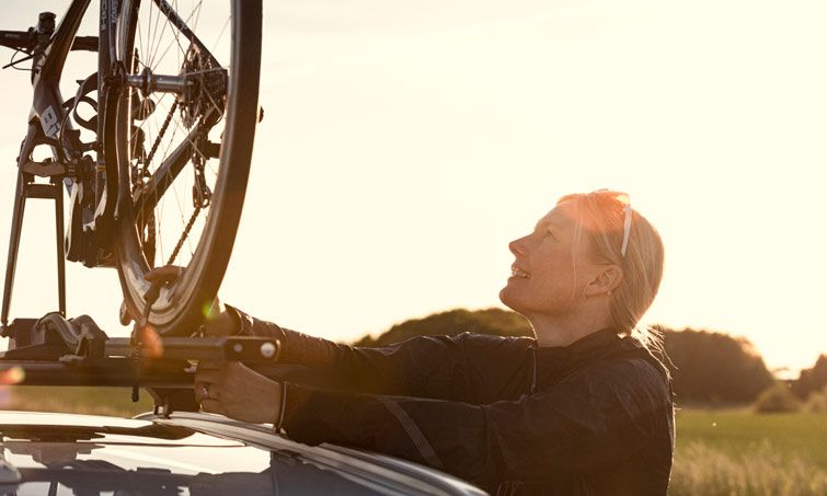 A woman loads her Thule Edge WingBar roof rack with a bicycle.