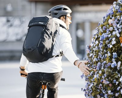 黒いサイクル用バックパックを背負って自転車を走らせ、花を撫でながら通り過ぎる男性。