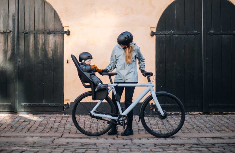 A woman tends to her baby in a Thule child bike seat on a blue bicycle. 