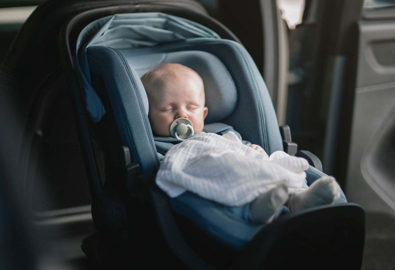 A baby sleeping in a Thule Maple infant car seat in mid-blue.