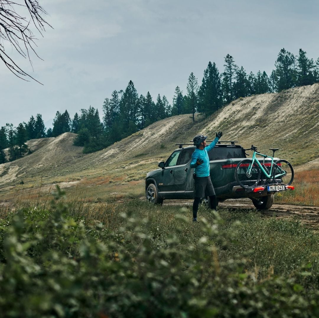A man wearing a bike helmet stands near a pick up truck with a bike mounted on a Thule Epos bike rack. 