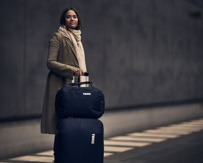 Женщина стоит на железнодорожной станции, держа чемодан на колесиках.
