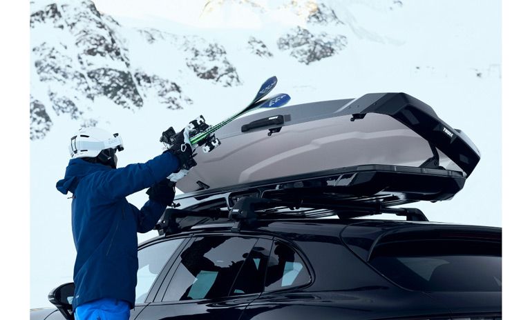 A close-up of a skier putting their skis into a Thule Vector rooftop cargo carrier.