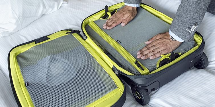 A close-up of someone packing an open Thule carry on luggage lying on a bed.