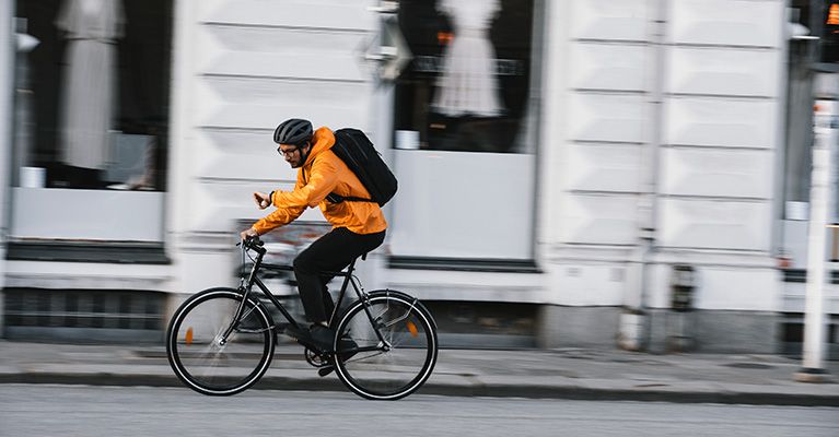 En mand cykler på en cykel med en Thule cykelrygsæk, mens han kigger på sit ur.