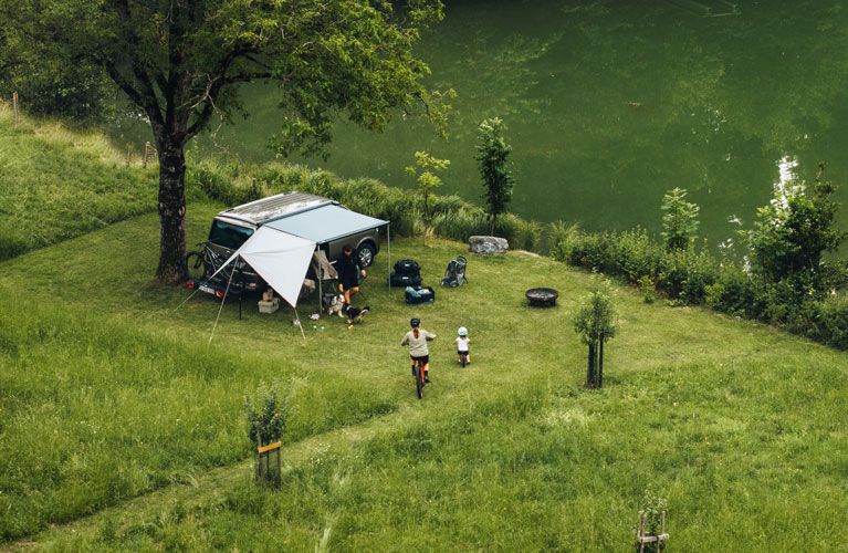 A bird’s eye view of a compact van with the Thule Subsola panels parked in the grass next to a lake.